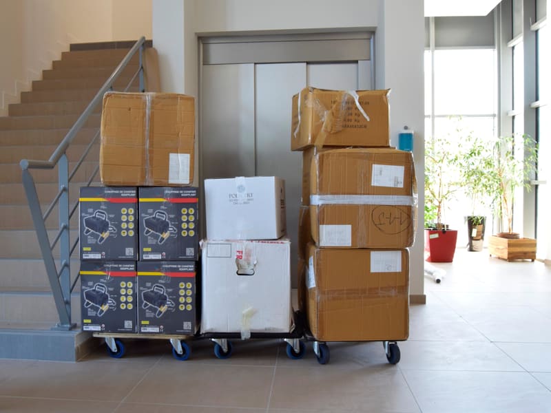 Wrapped cartons and crates stacked on wheeled dollies, staged indoors